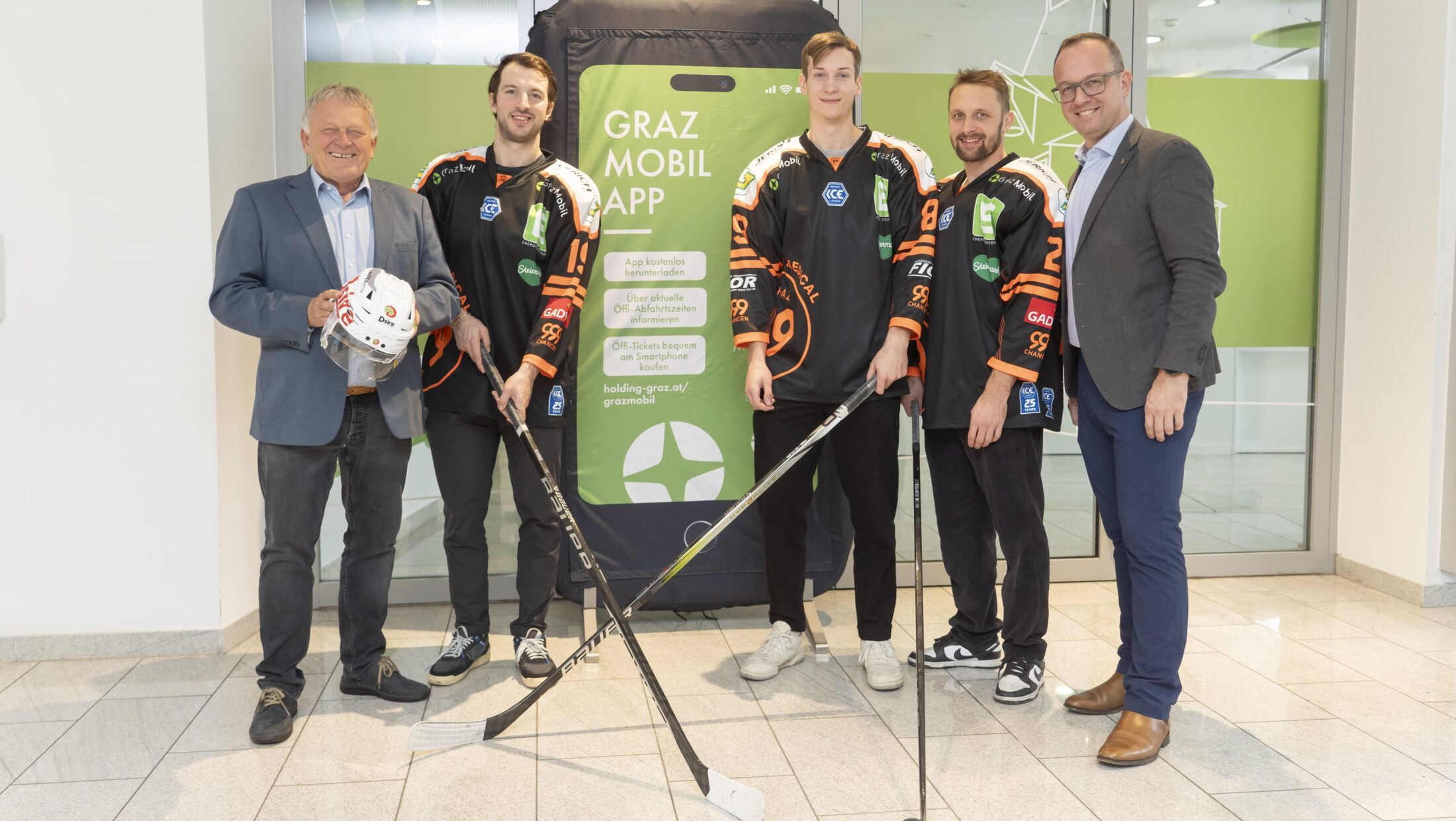 Five men stand in front of a large phone prop advertising the Graz Mobil App.