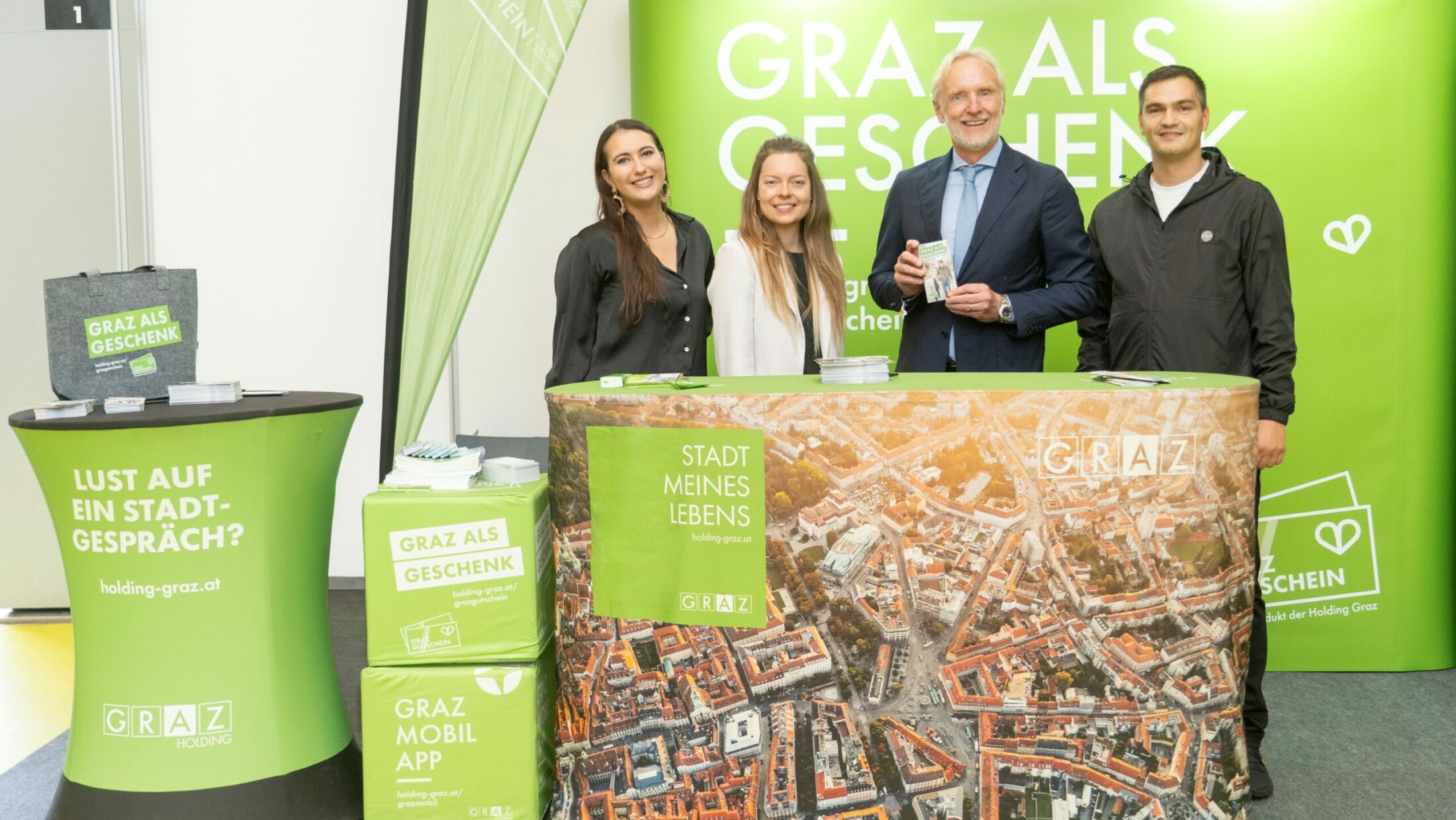 Vier Personen stehen vor einem Stand mit dem Slogan „Graz als Geschenk"