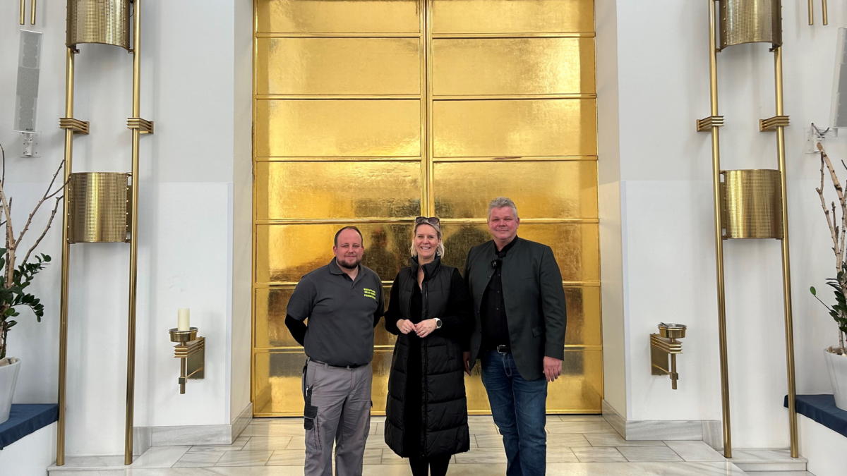 Drei Personen vor einer goldenen Tür in Graz, lächelnd.